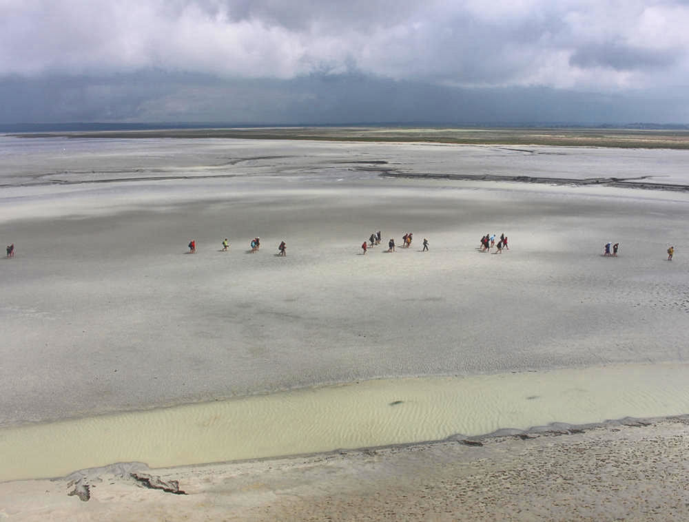 People walking along the clay sands of the bay around Mont-Saint-Michel. Credit tiger rus