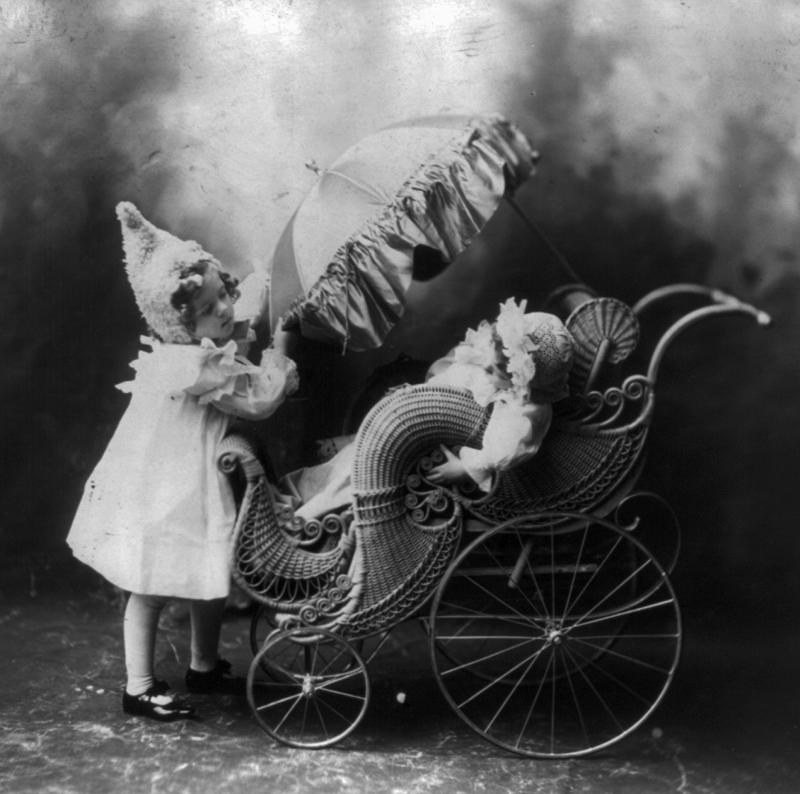 c 1901. Sibling making adjustments to a pram's sun shade