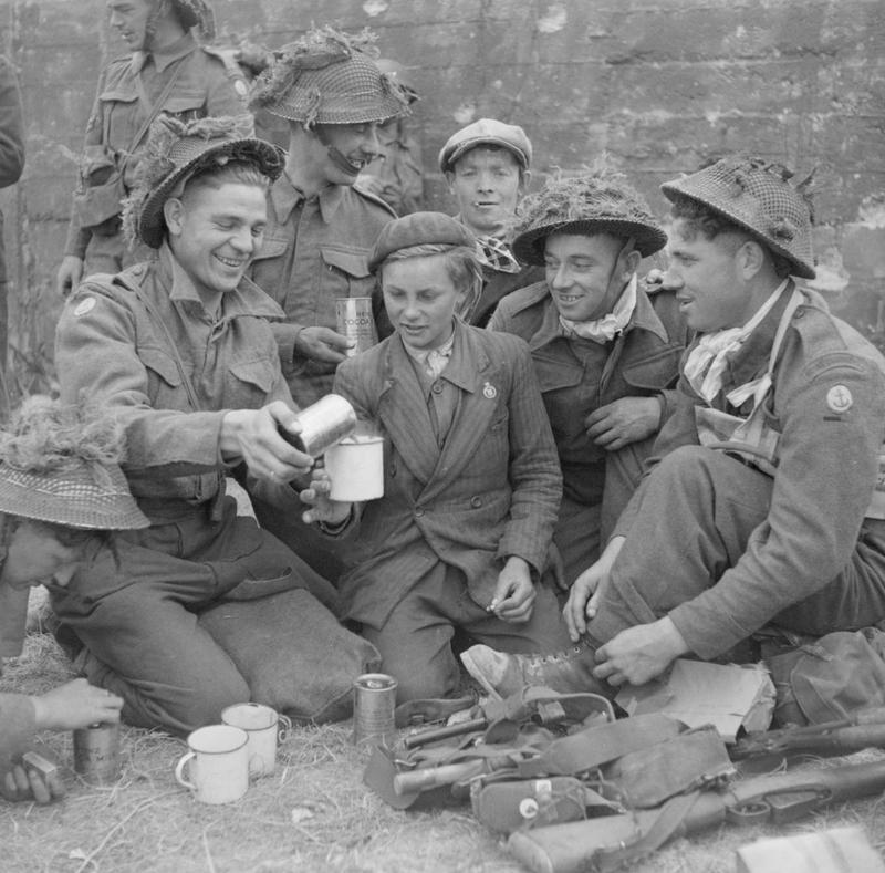 Royal Engineers serving with a 50th Division Beach Group share cocoa with a French boy in the village of Ver-sur-Mer