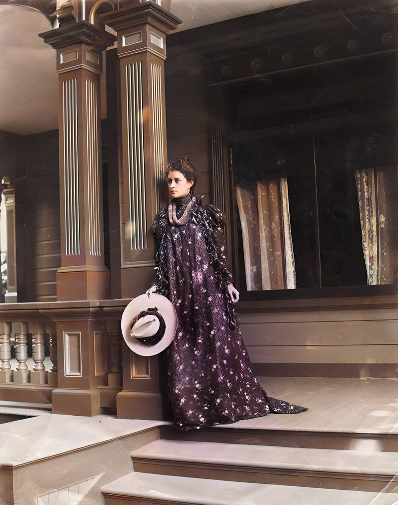 Princess Kaiulani standing on top of steps on the porch of her house at ʻĀinahau; wearing the holoku and a lei