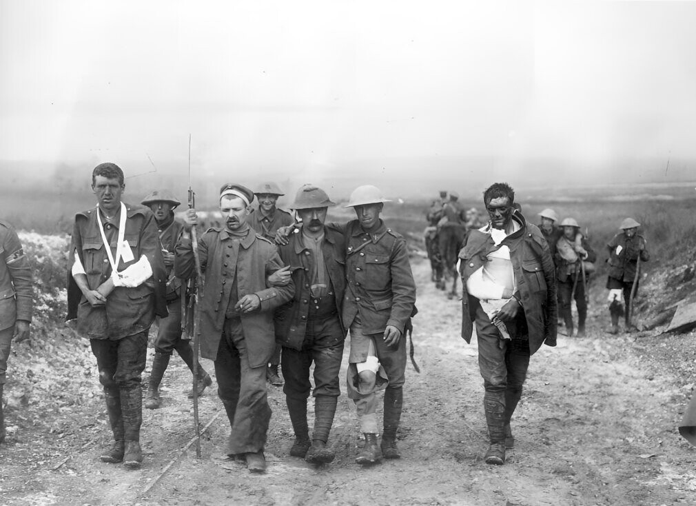 A German prisoner helps British wounded make their way to a dressing station near Bernafay Wood following fighting on Bazentin Ridge, 19 July 1916, during the Battle of the Somme.
